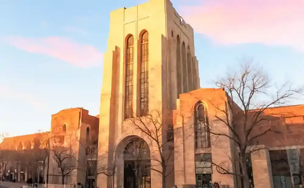 A tall, stone building with arched windows and a pointed roof, bathed in warm sunset light.