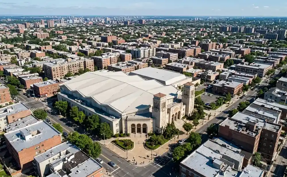 Aerial view of a large, light-colored domed building surrounded by city blocks and trees.