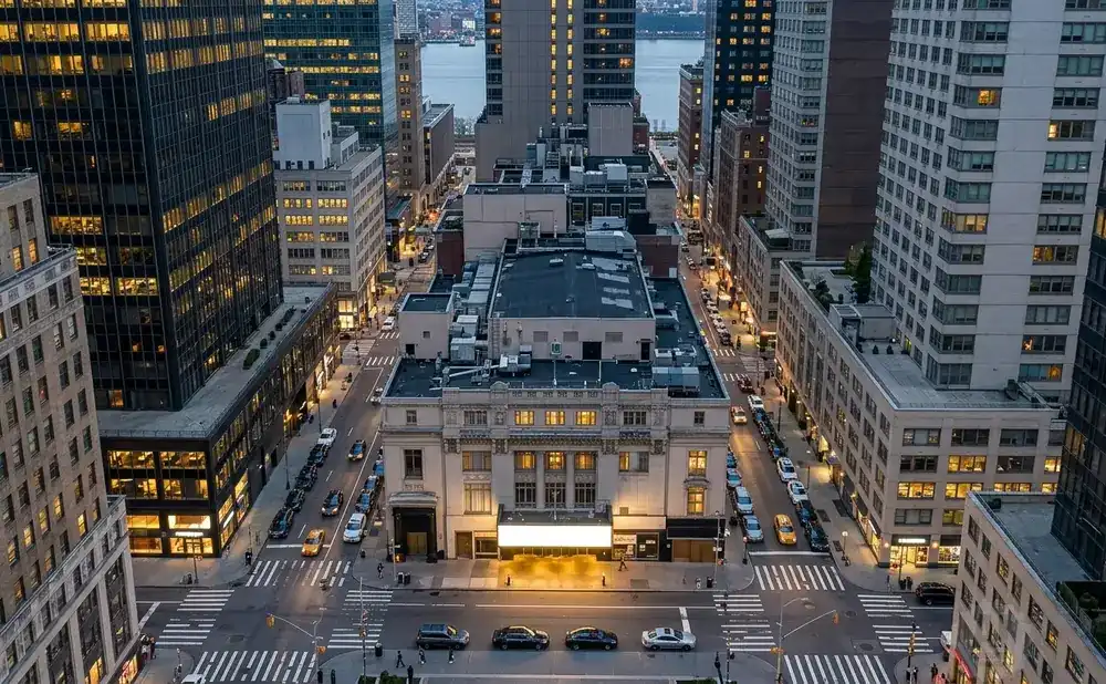 Aerial view of a city street with tall buildings, cars, and pedestrians at dusk.