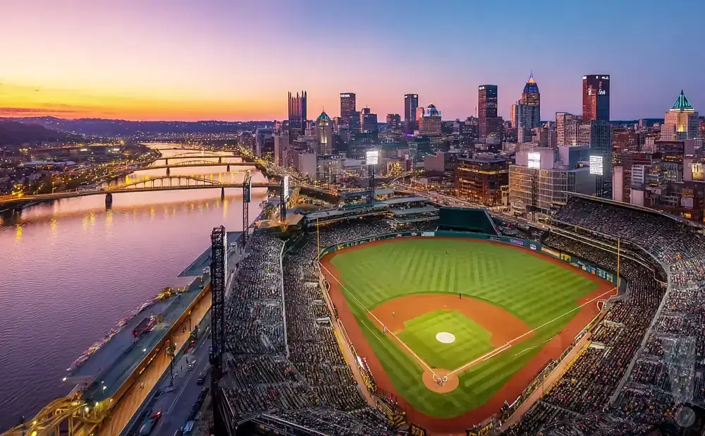 Aerial view of PNC Park baseball stadium in Pittsburgh, with downtown skyline and bridges at sunset.