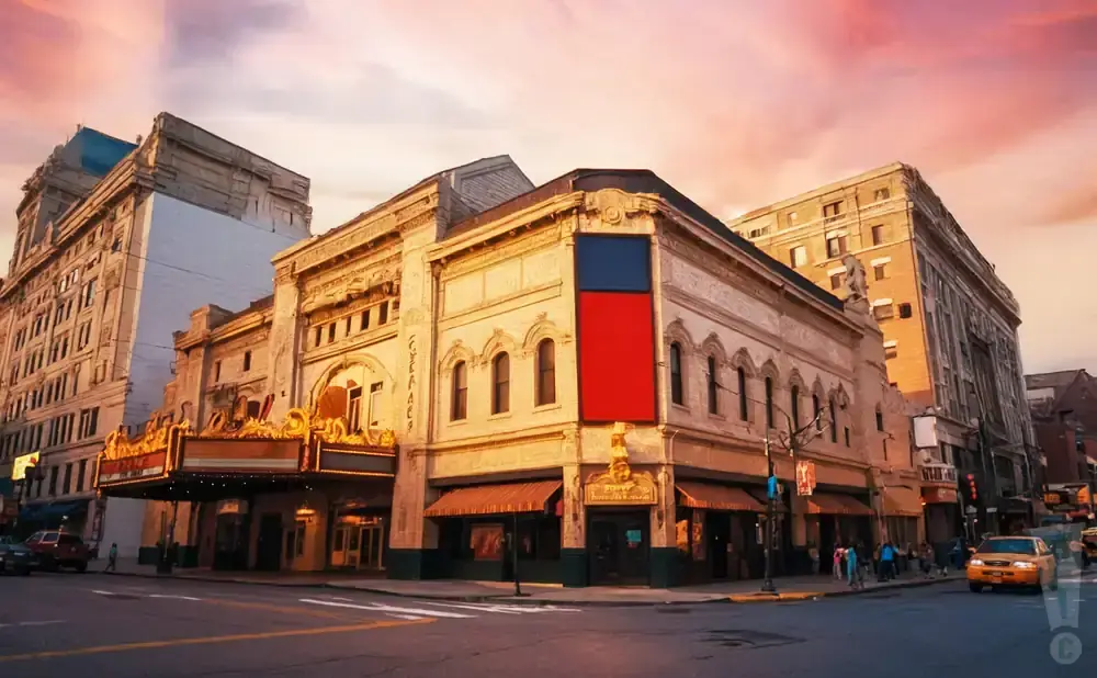 A vintage theater glows with marquee lights against a vibrant sunset sky, with surrounding brick buildings.