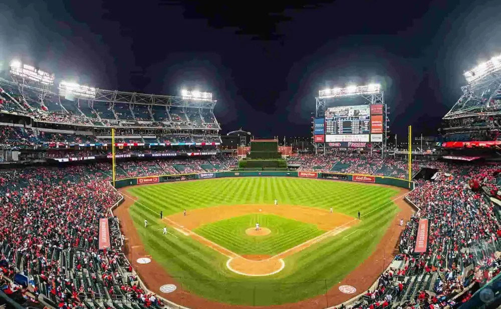 A baseball stadium at night, with bright lights illuminating the field and a packed crowd in the stands.