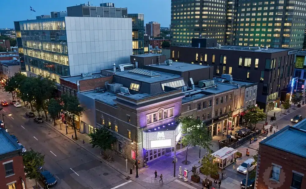 Aerial view of a street with buildings, cars, and people at dusk.