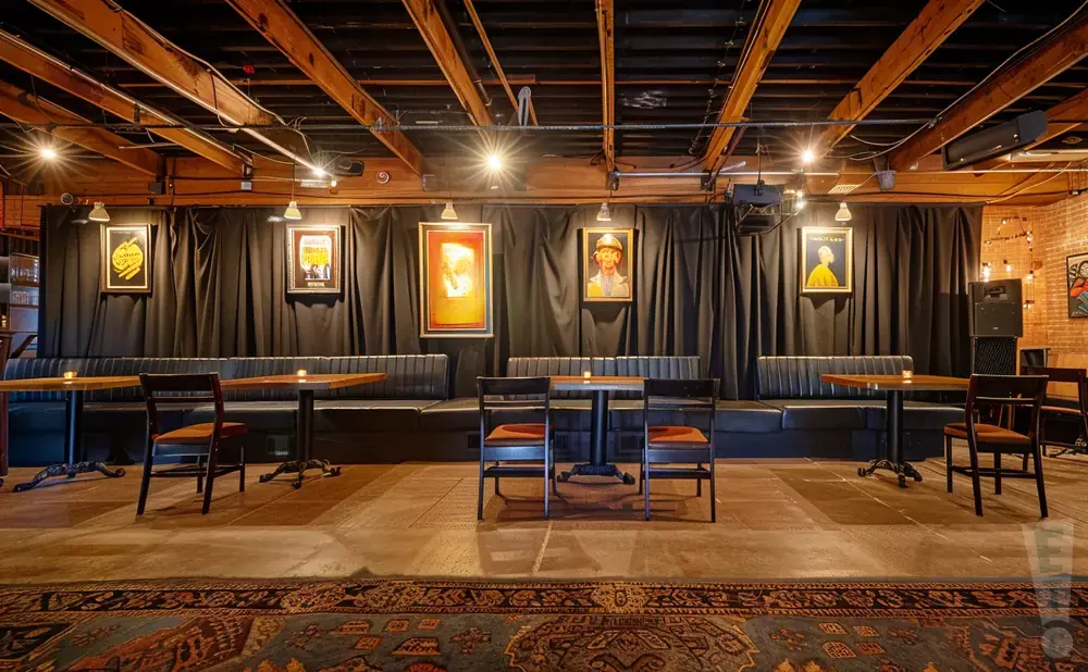 Interior of a restaurant with black booths, wooden tables, and framed art on a dark curtained wall.