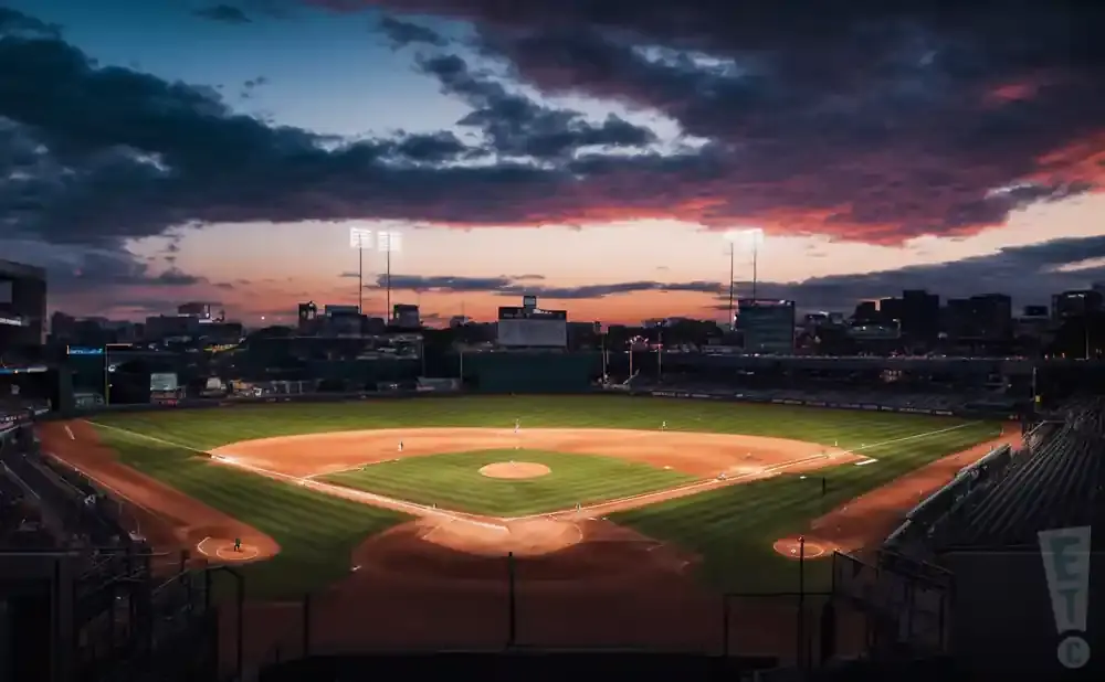 A baseball field at sunset with dramatic clouds and city lights.