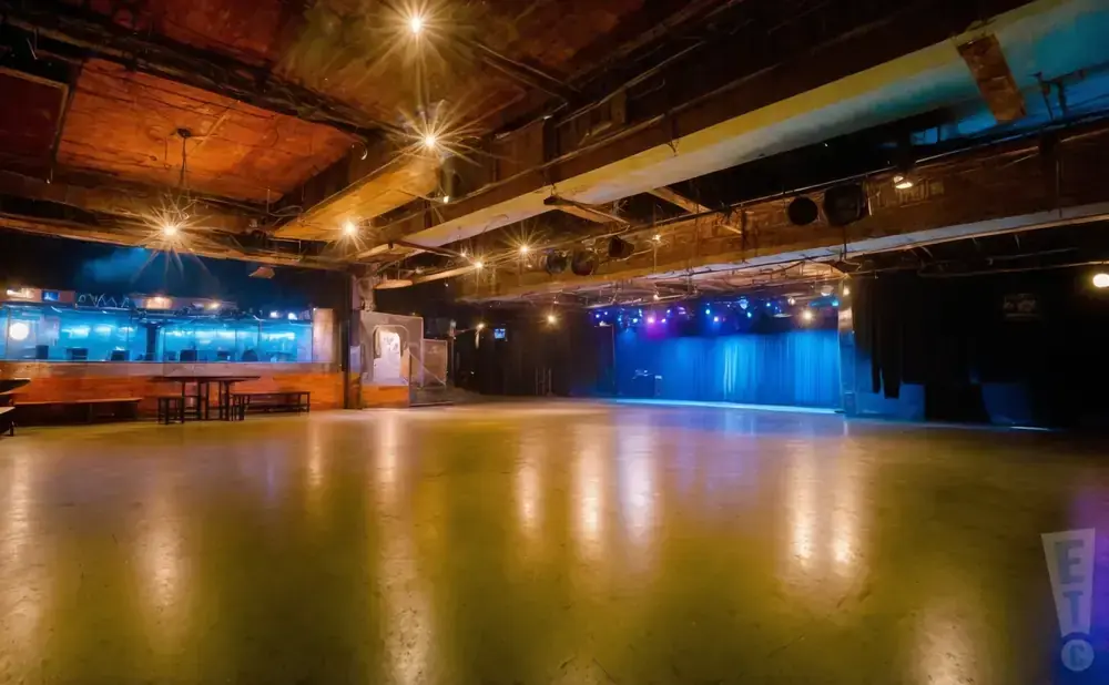 A wide, empty dance floor in a club, with a stage and seating area in the background.