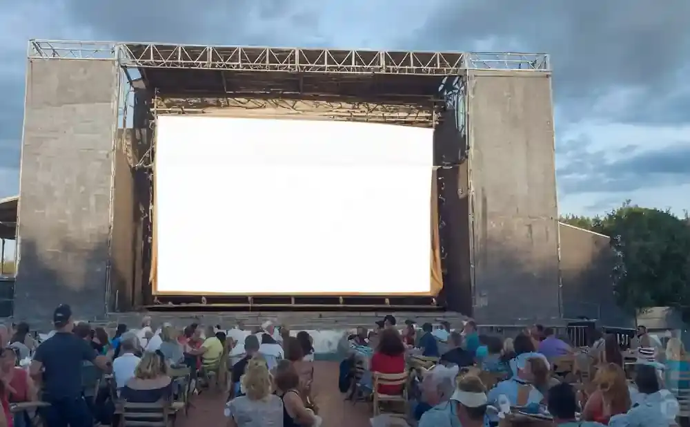 Outdoor movie screen with audience sitting in chairs.