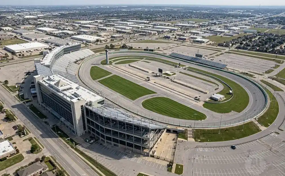 Aerial view of a race track complex with grandstands, parking lots, and surrounding industrial buildings.