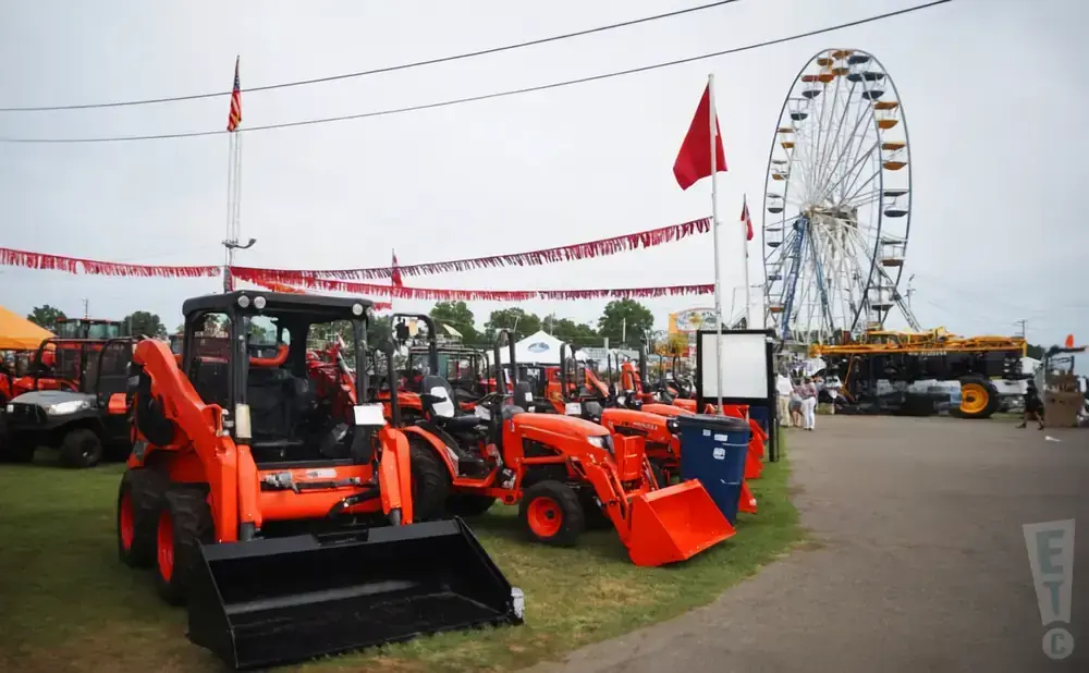 Orange tractors and equipment displayed under red pennant banners with a Ferris wheel in the background.
