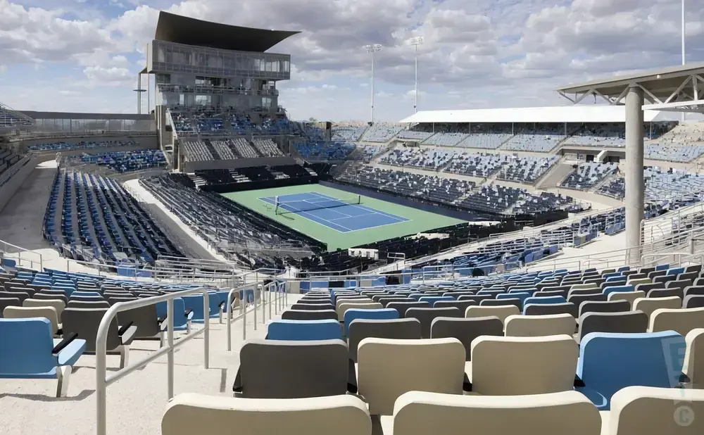 An empty tennis stadium with blue and gray seats surrounding a green court.