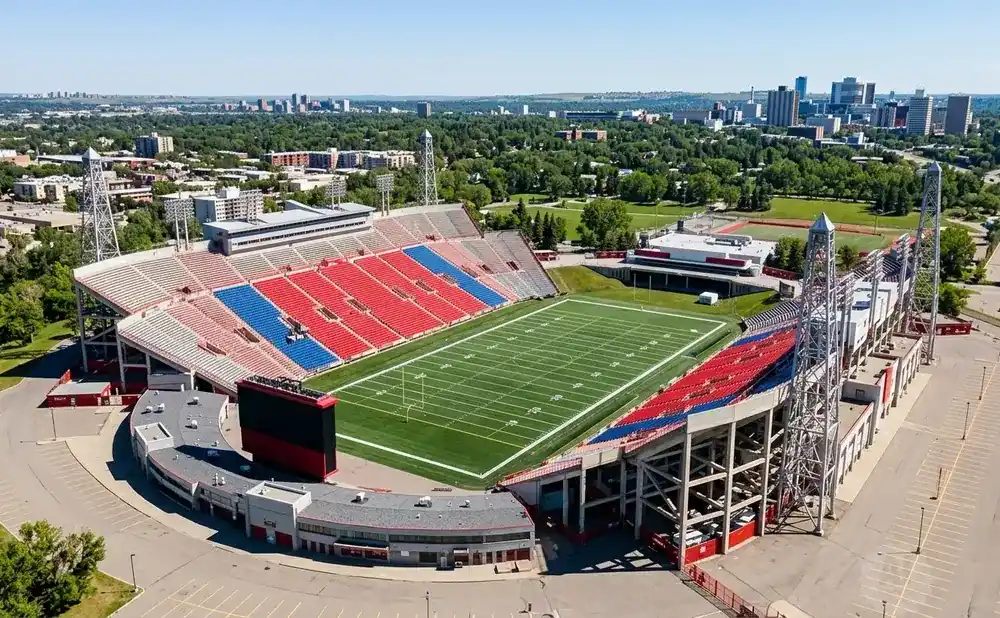 Aerial view of a stadium with red and blue seats, a green football field, and a city skyline in the distance.