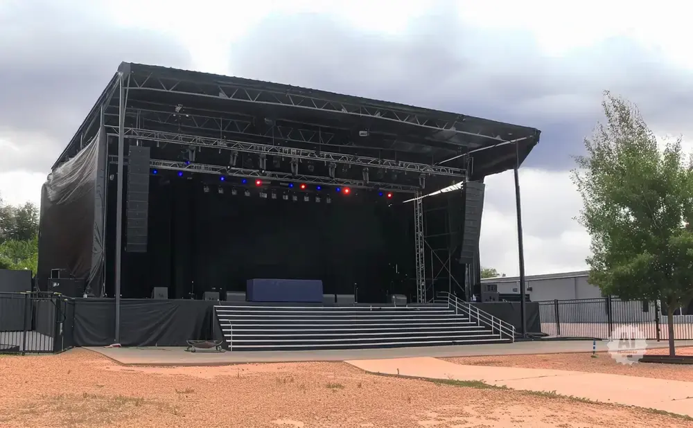 An outdoor concert stage with speakers, lighting, and a large black backdrop.