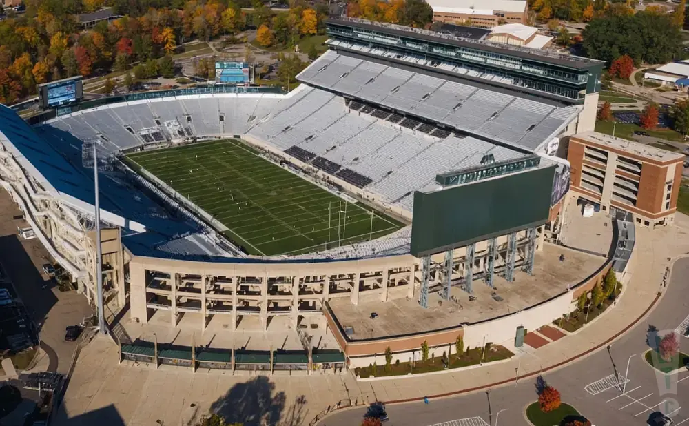 Aerial view of an empty football stadium with green field and stands under a clear sky.