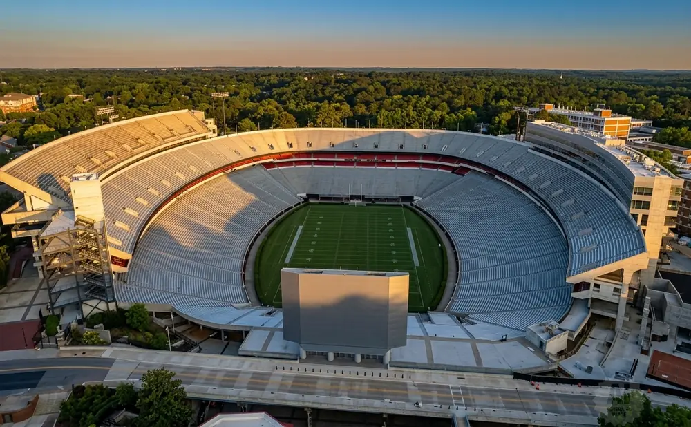 Aerial view of an empty football stadium during golden hour, with a green field and empty seats.
