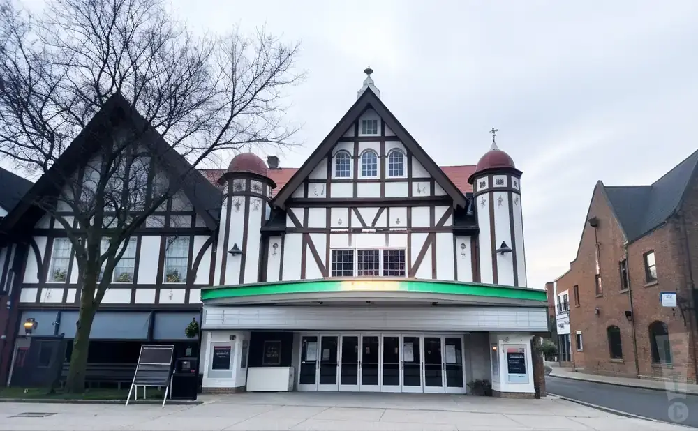 Tudor-style theater with arched windows and a green marquee in front of a brick building.