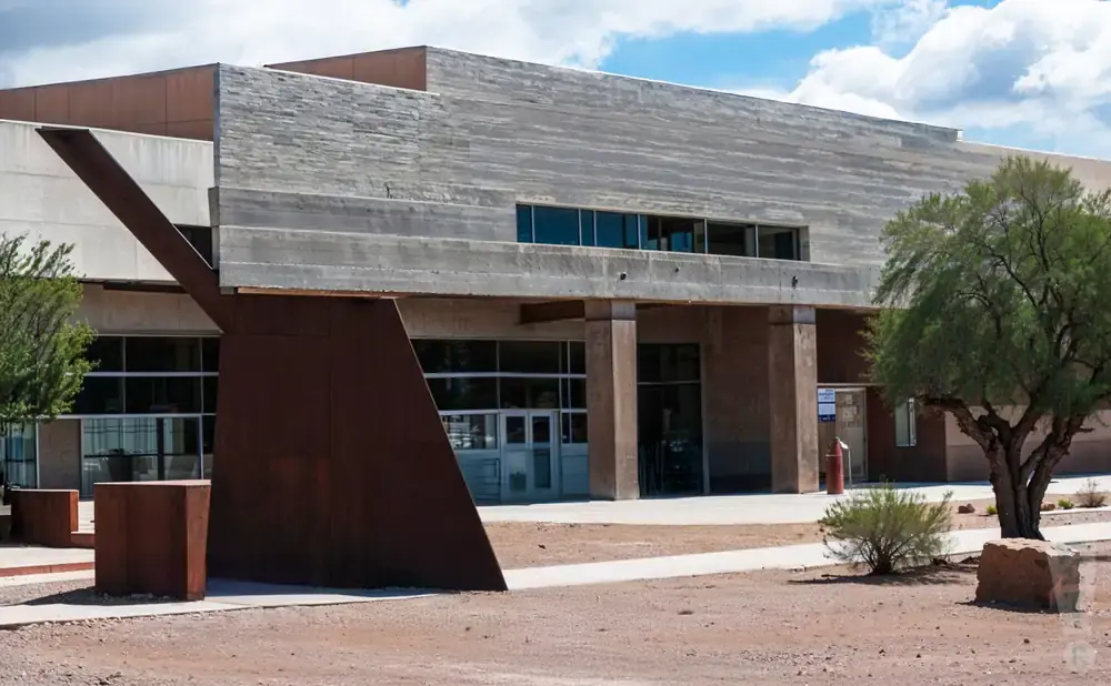 Modern building with concrete and rust-colored metal accents, featuring large windows and a tree.