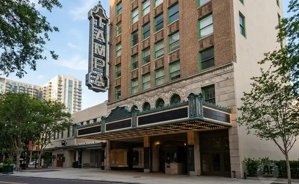 The historic Tampa Theatre marquee, illuminated with lights, stands against a brick building and a light-colored wall.