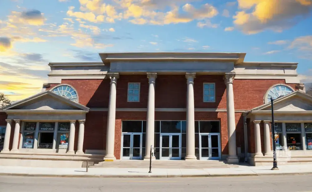 Classical brick building with columns and arched windows under a cloudy sky.