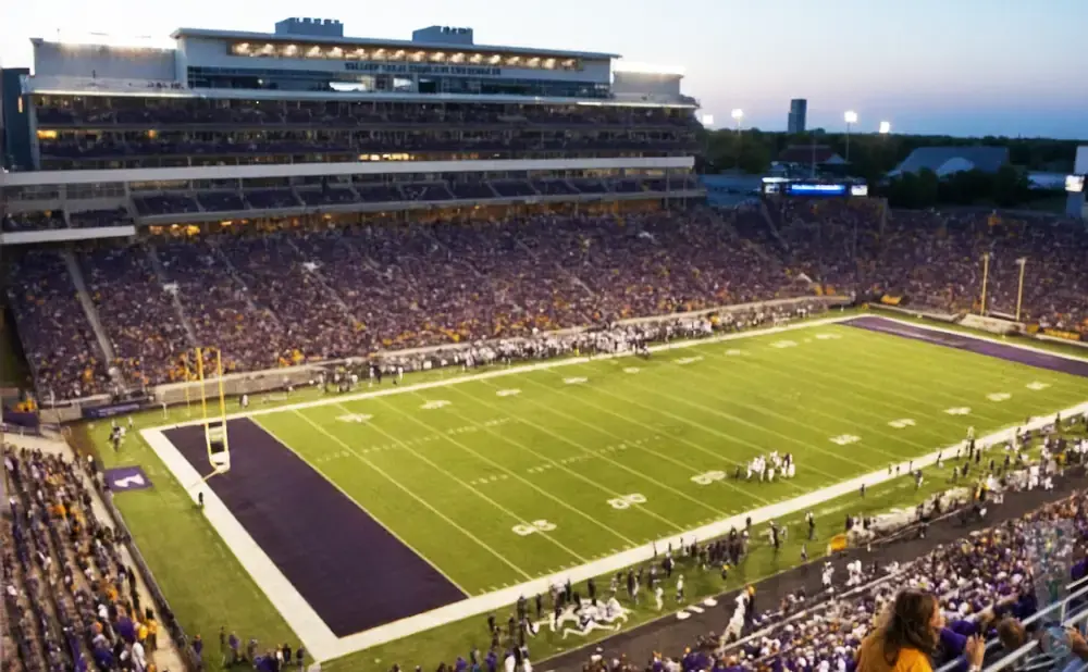 A football stadium filled with purple-clad fans at dusk.
