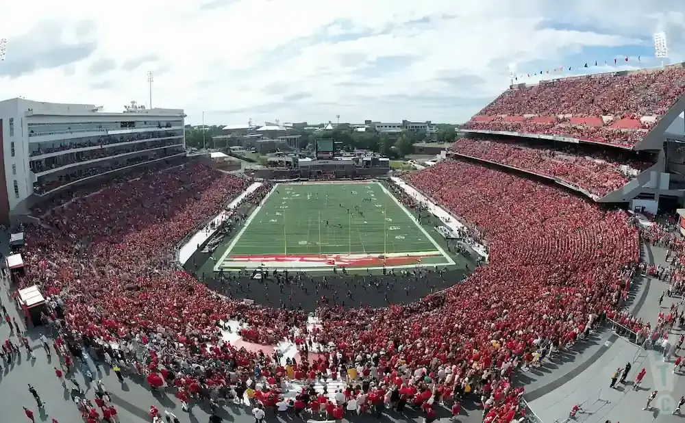 An aerial view of a crowded football stadium, with fans in red filling the stands surrounding the green field.