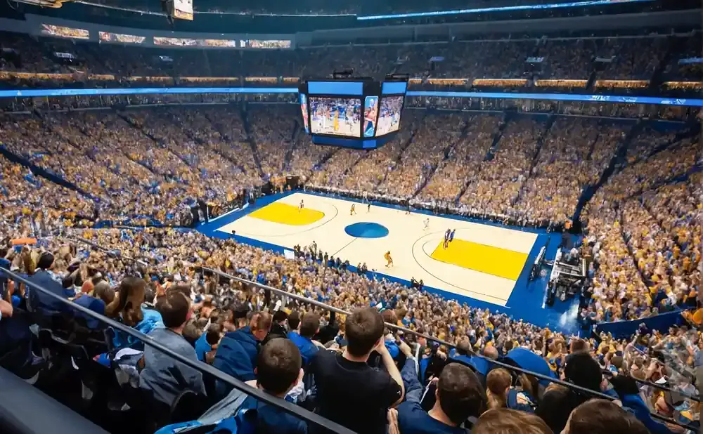 Aerial view of a crowded basketball arena with fans in gold and blue, and a game in progress on the court.