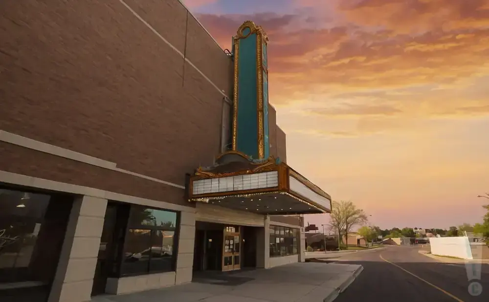 A vintage movie theater marquee with a large illuminated sign against a colorful sunset sky.
