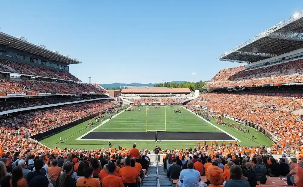 Fans in orange fill a stadium during a sunny football game.