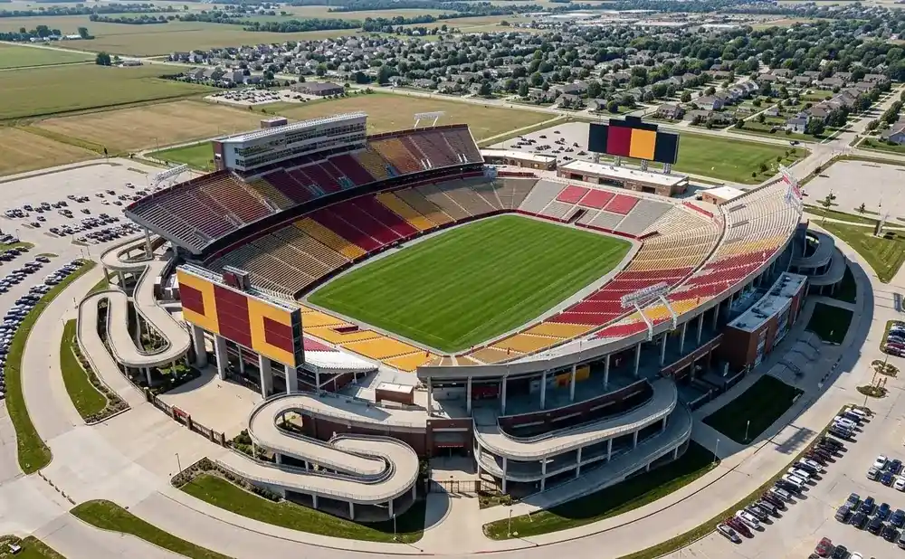 Aerial view of a football stadium with a bright green field, surrounded by parking lots and a suburban neighborhood.