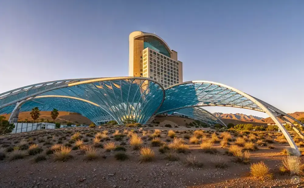Modern hotel with a large, blue, arched canopy in a desert landscape at sunset.