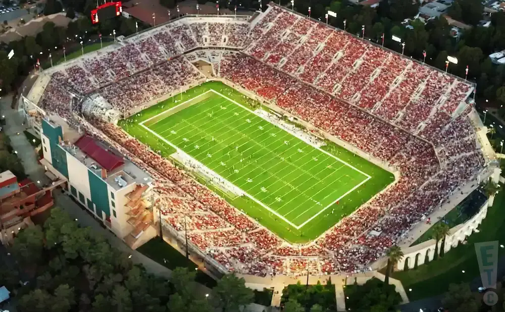 Aerial view of a crowded football stadium with a green field and red-seated stands.