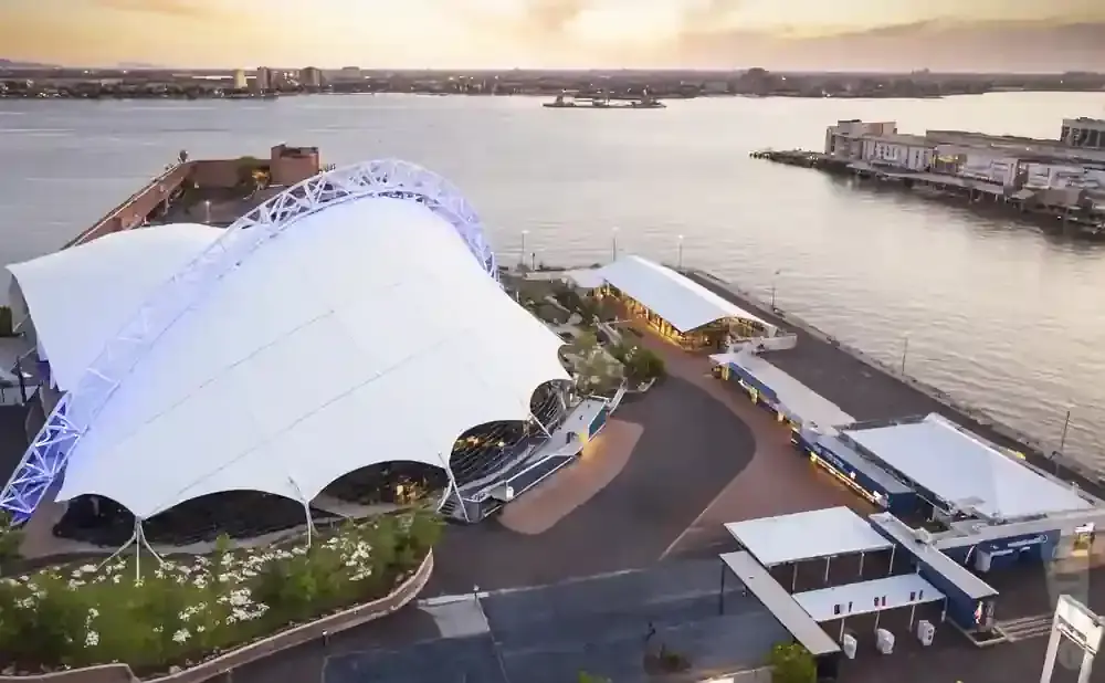 Aerial view of a waterfront venue with a large white tensile canopy and surrounding buildings.