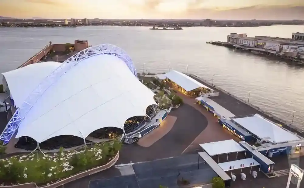 Aerial view of a waterfront venue with a large white tent structure and nearby buildings.