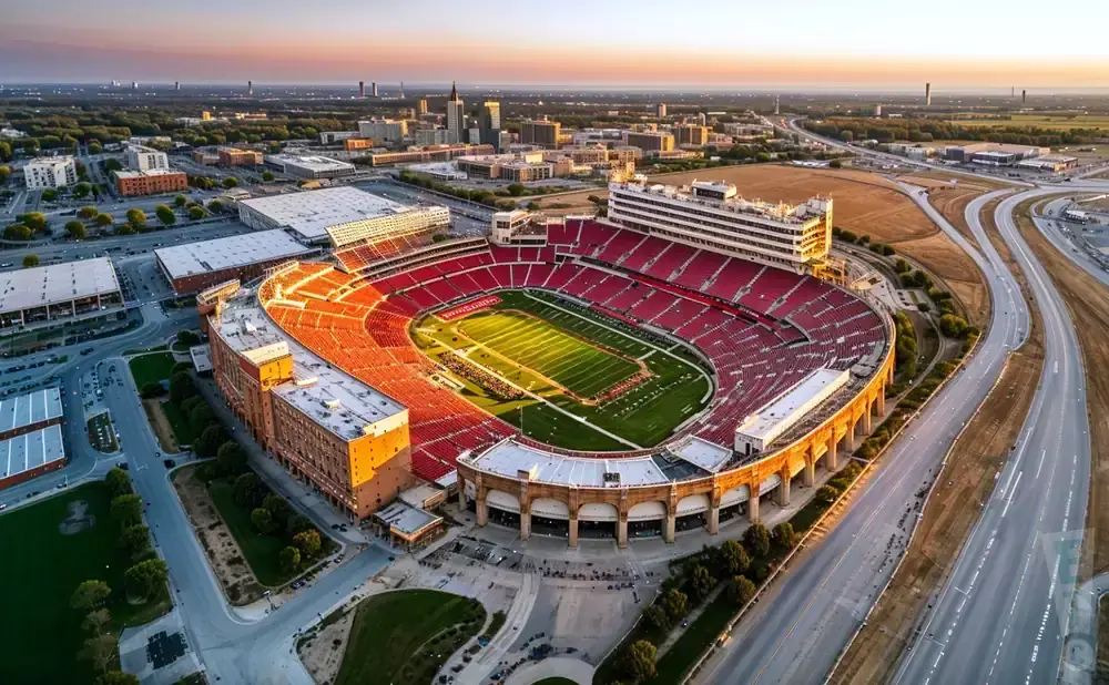 Aerial view of a large, red-seated football stadium at sunset with a cityscape in the background.