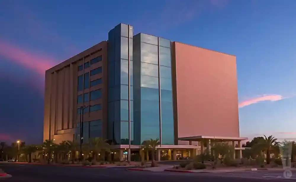 A modern, multi-story building with beige and glass facades at dusk with pink and blue clouds.