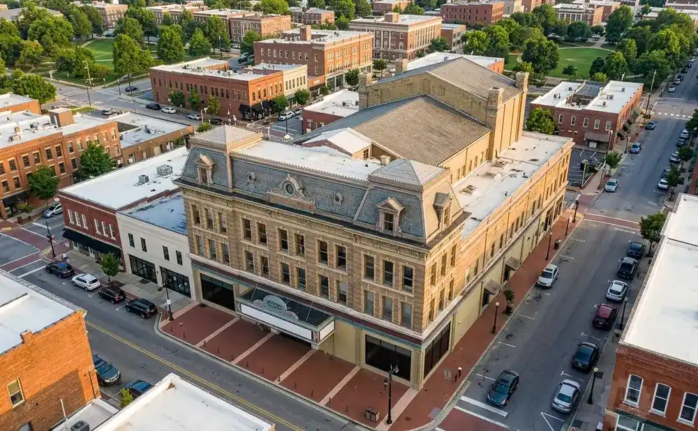 Aerial view of a historic theater building on a tree-lined street in a town square with surrounding brick buildings.