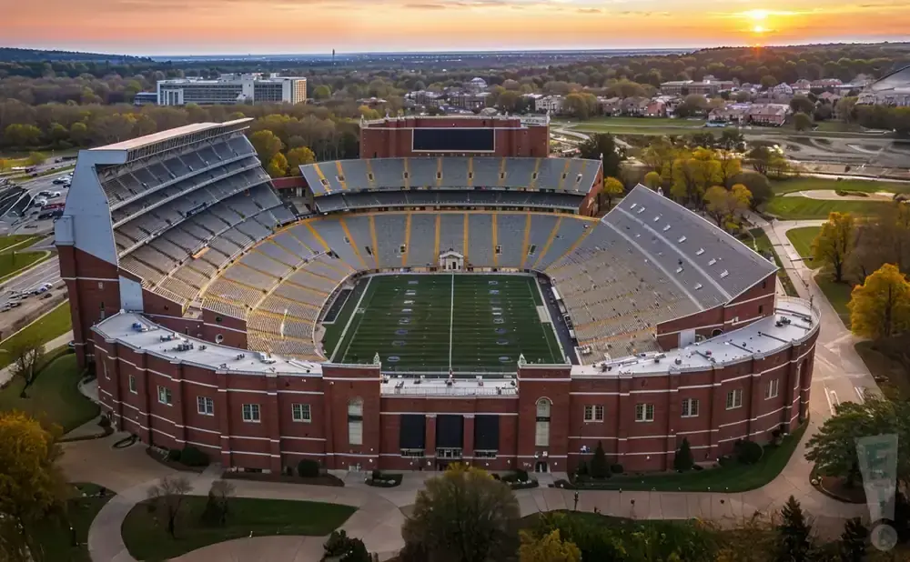 Aerial view of a brick stadium with a football field and yellow-seated stands at sunset.