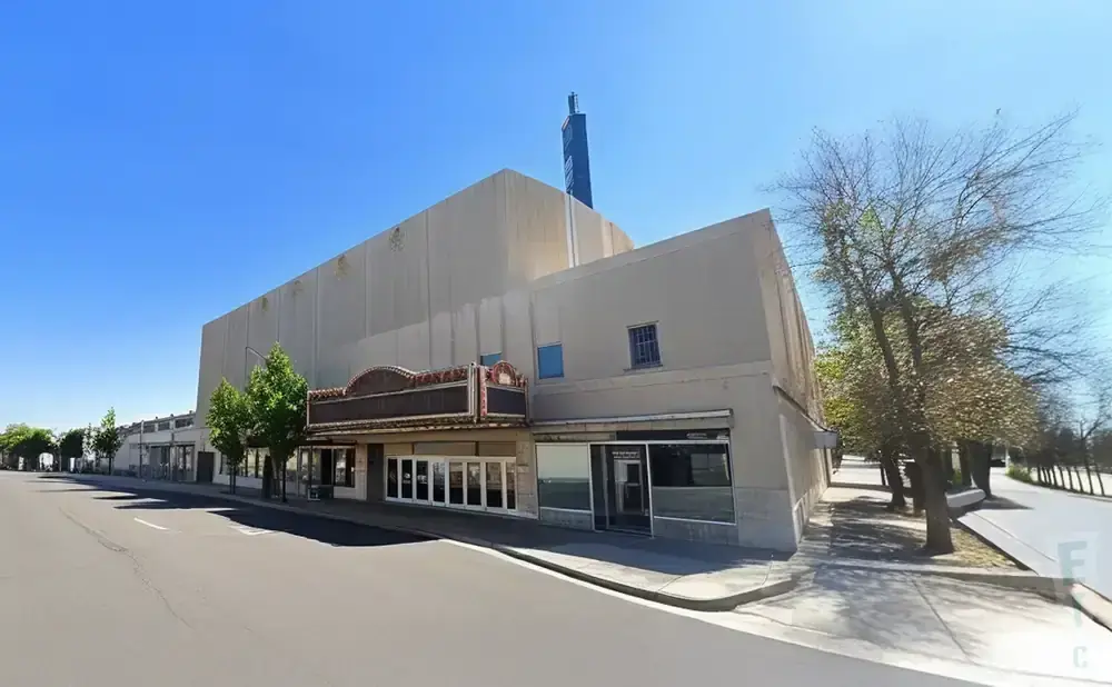 Exterior view of a large, beige building with a vintage marquee and several windows, under a clear blue sky.