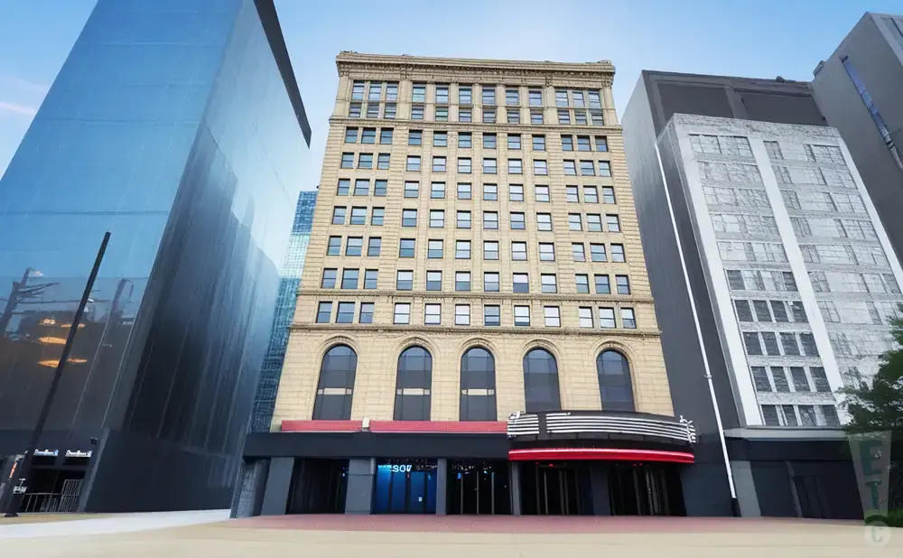 A vintage tan building stands between two modern glass skyscrapers under a clear blue sky.