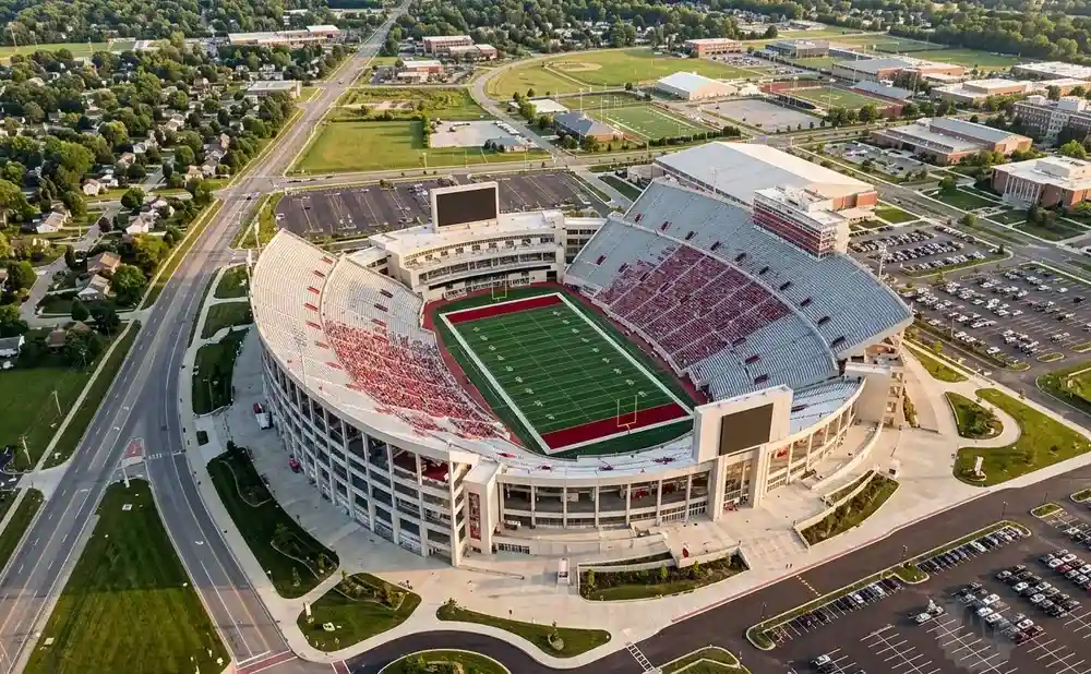 Aerial view of a large, open-air football stadium with red seating and a green field.