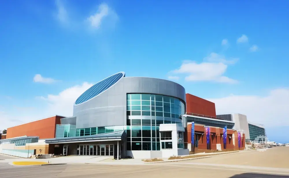 Modern building with a curved glass facade and a large, sloped roof under a blue sky with clouds.