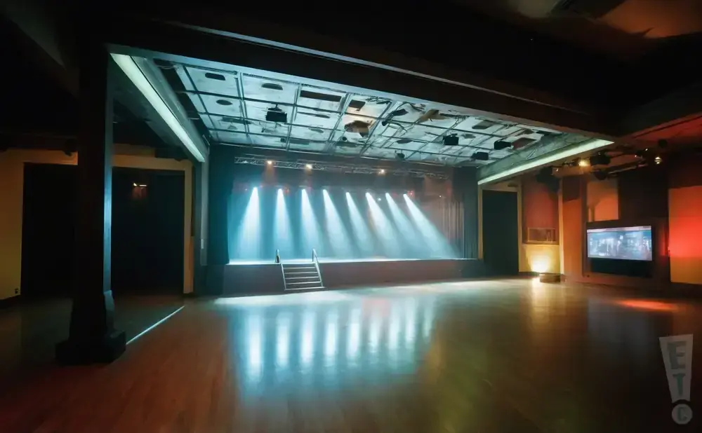 An empty indoor stage with spotlights and a polished wooden floor reflecting the lights.