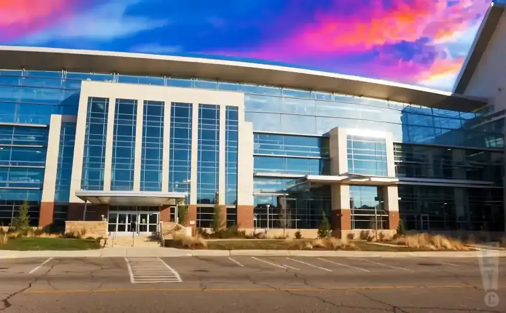 A modern glass building with a dramatic sunset sky.