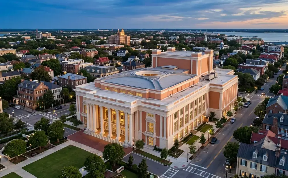 An aerial view of a large, salmon-colored building with columns, surrounded by historic homes and trees, at dusk.