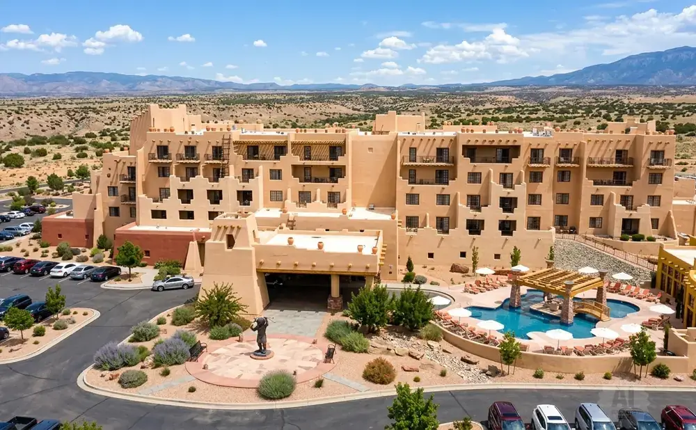 Aerial view of a tan, multi-story hotel with southwestern architecture, featuring a pool and parking lot.