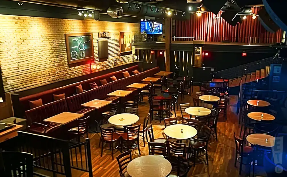 Interior of a dimly lit venue with brick walls, booth seating, and many tables and chairs.