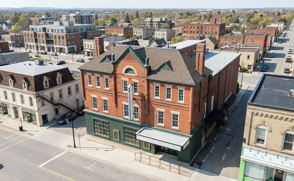 Aerial view of a brick building with a green facade and a marquee, in a town with other buildings and streets.