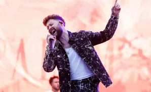 A male singer belts into a microphone while raising his hand in the air.