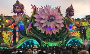A giant flower stage at an outdoor festival with two large statues of women on either side.