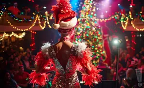 A performer in a sparkly red outfit and Santa hat, with a Christmas tree and audience in the background.