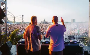Two DJs perform on stage at a music festival to a large cheering crowd.